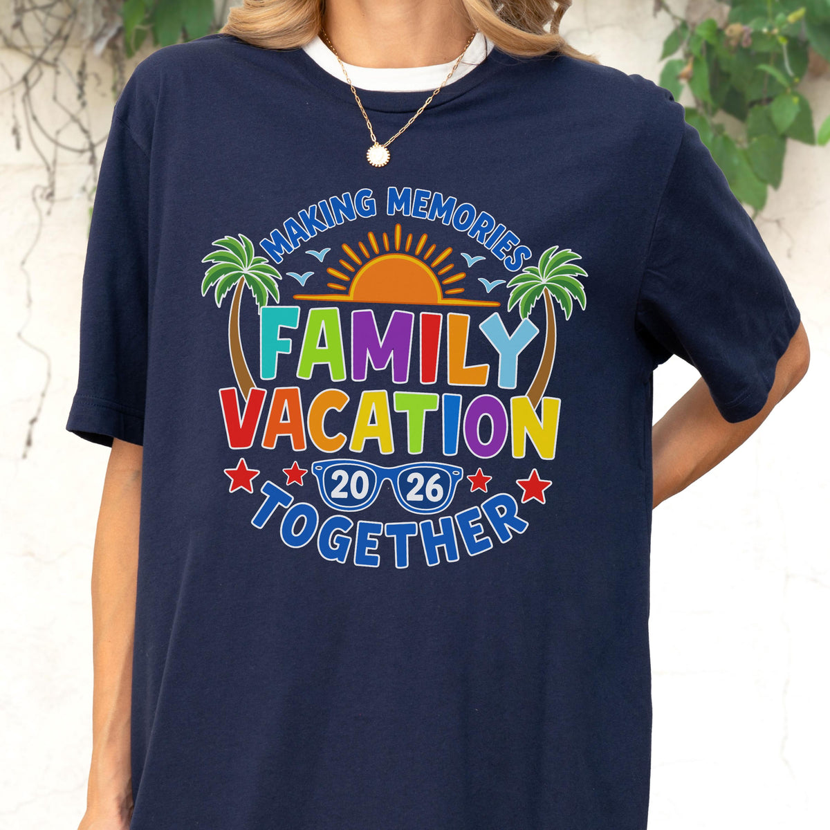 May include: A navy blue t-shirt featuring a colorful graphic with the text "MAKING MEMORIES FAMILY VACATION TOGETHER" and "2026". The design includes a bright orange sun, green palm trees, blue sunglasses, and red stars, creating a vibrant summer theme.