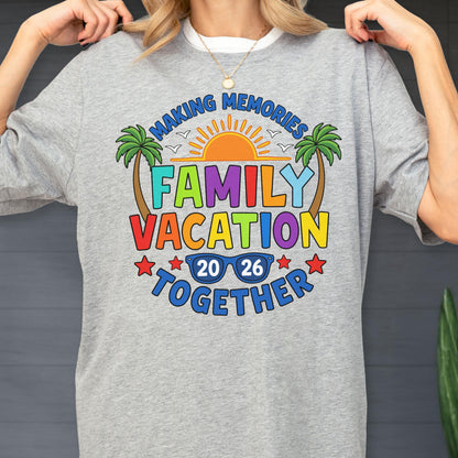 May include: A heather gray t-shirt featuring a colorful graphic with the text "MAKING MEMORIES FAMILY VACATION TOGETHER 20 26". The design includes a bright orange sun, two palm trees, and blue sunglasses, all accented by small red stars.
