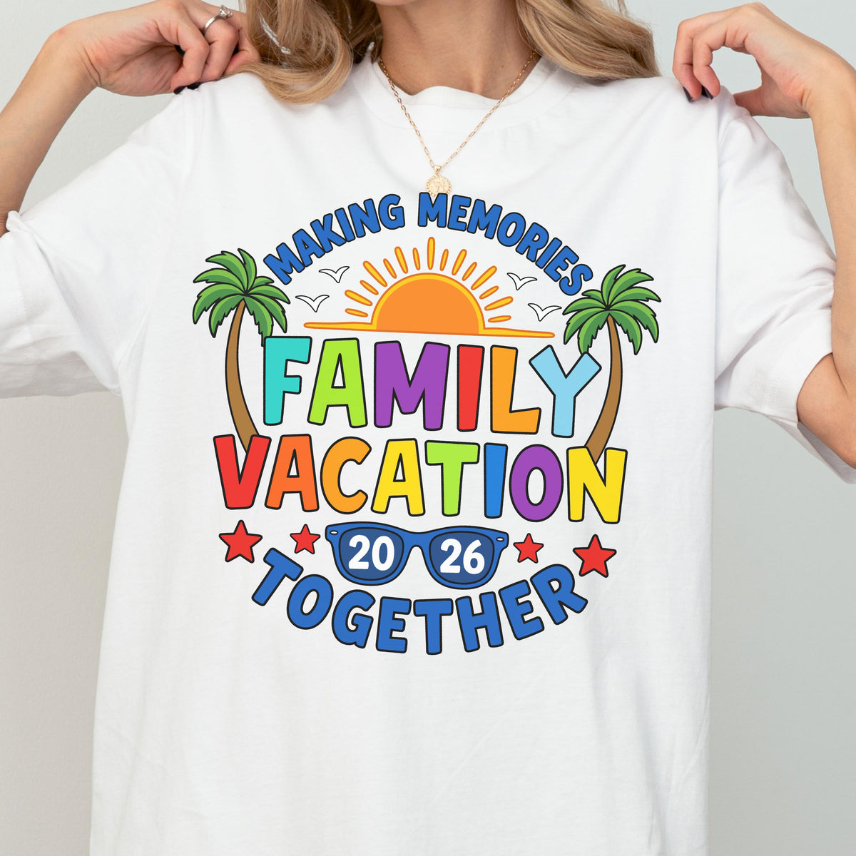 May include: A white t-shirt featuring a colorful graphic with the text "MAKING MEMORIES FAMILY VACATION TOGETHER 20 26". The design includes a bright orange sun, green palm trees, blue sunglasses, and red stars, creating a vibrant summer-themed print.
