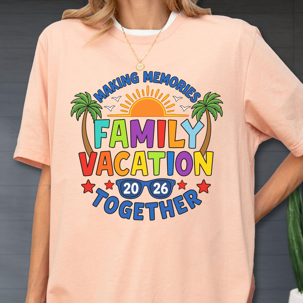 May include: A peach-colored t-shirt featuring a graphic with the text "MAKING MEMORIES FAMILY VACATION TOGETHER 20 26". The design includes a yellow sun, two green palm trees, blue sunglasses, and red stars, all printed in a vibrant, multi-colored style.