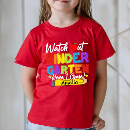 May include: A bright red short-sleeved t-shirt featuring the white text Watch out, a red apple icon, and the colorful text KINDERGARTEN Here I Come! with a yellow pencil graphic containing the name Amelia in black text on the front.