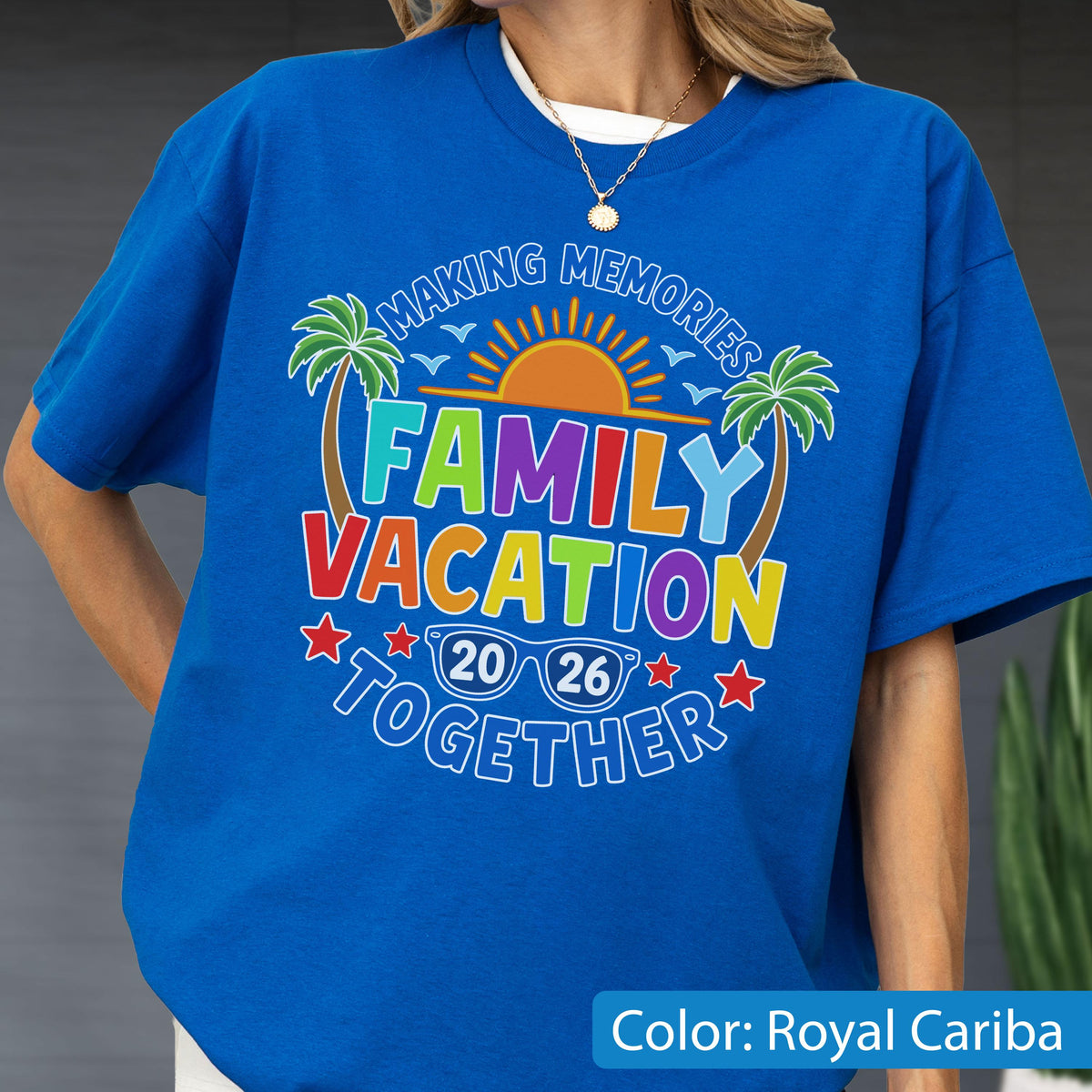 May include: A royal blue t-shirt featuring a graphic print with the text "MAKING MEMORIES FAMILY VACATION TOGETHER 20 26". The design includes a yellow sun, green palm trees, blue birds, and white sunglasses. A thin gold chain necklace is worn around the neck.