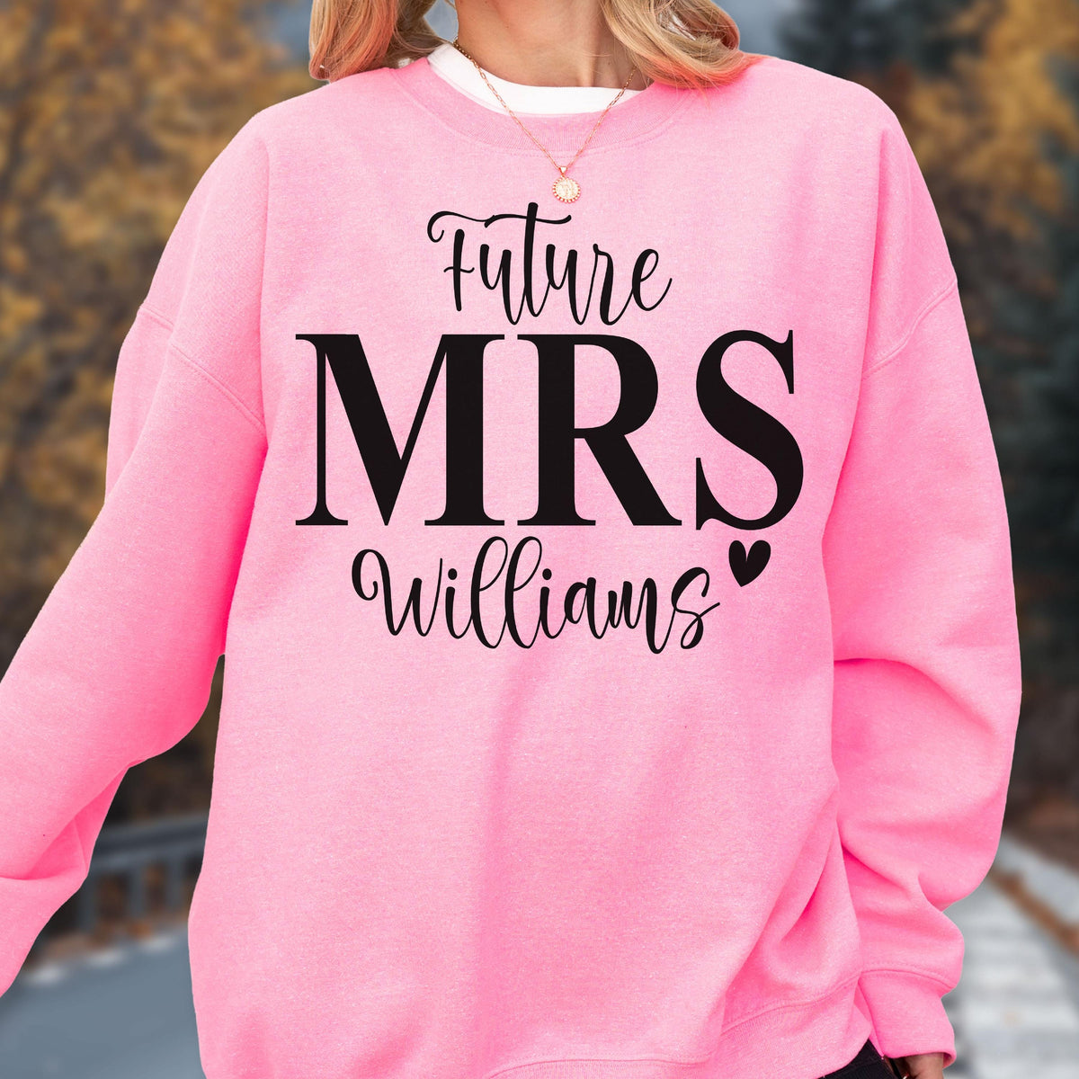May include: A bright pink crewneck sweatshirt featuring black text that reads Future MRS Williams with a small black heart icon. The garment has long sleeves and a ribbed neckline, showcasing a bold graphic design printed on the front center.