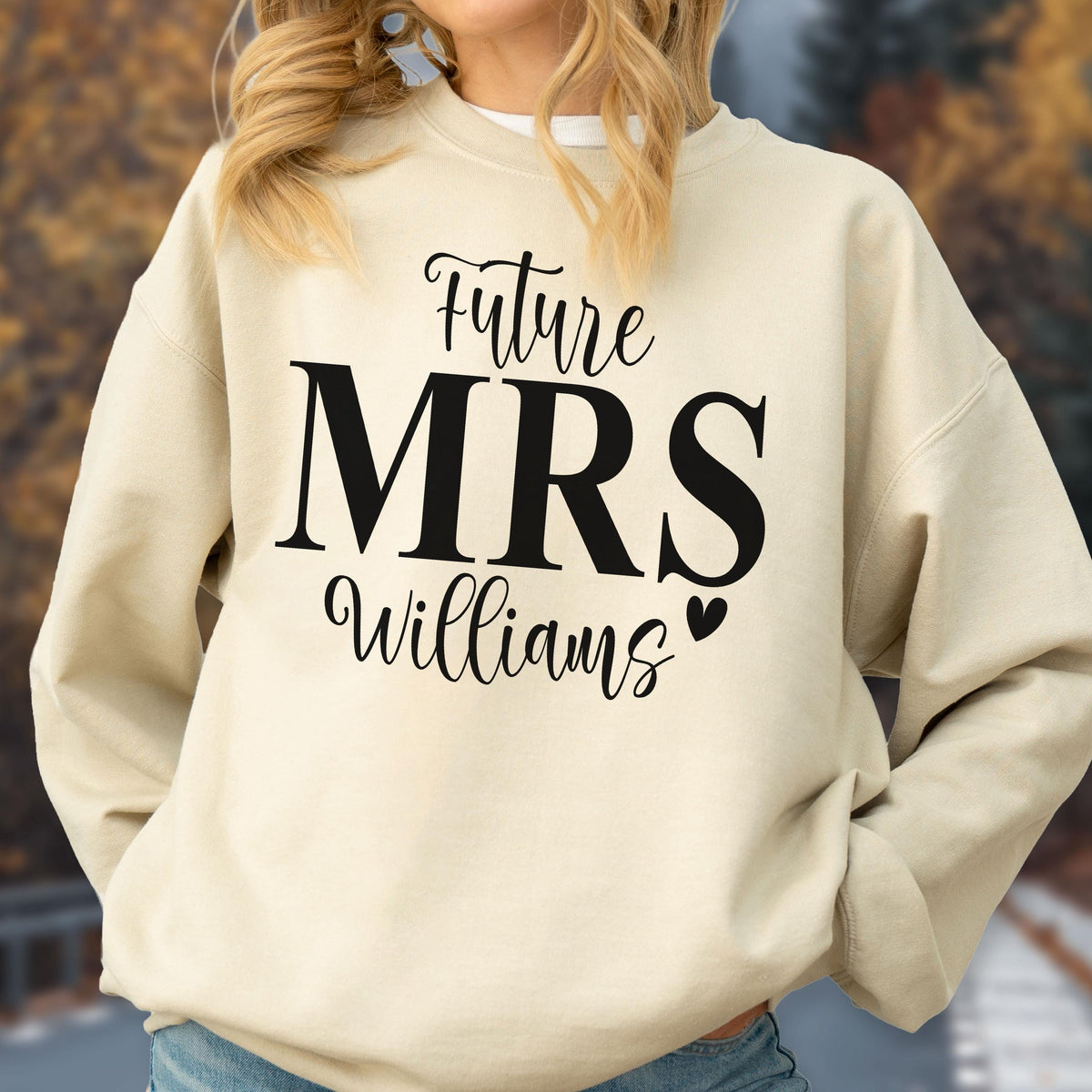 May include: A beige crewneck sweatshirt featuring black text that reads Future MRS Williams with a small heart icon. The garment has long sleeves, a ribbed collar, and a relaxed fit, showcasing a clear graphic print on the front chest area.