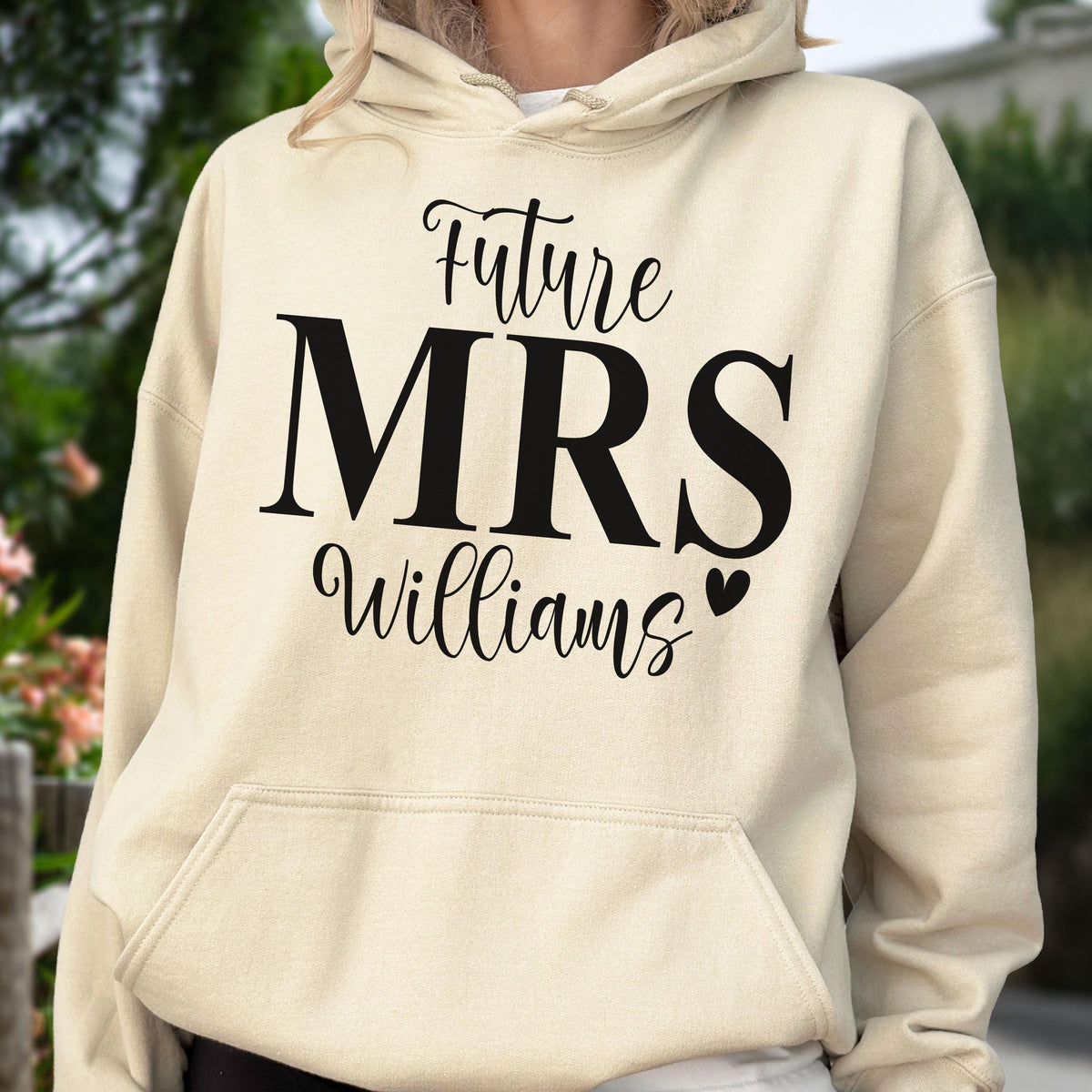 May include: A cream-colored hooded sweatshirt featuring black text on the front that reads Future MRS Williams with a small heart icon. The garment includes a front kangaroo pocket, long sleeves, and a drawstring hood with matching cream cords.