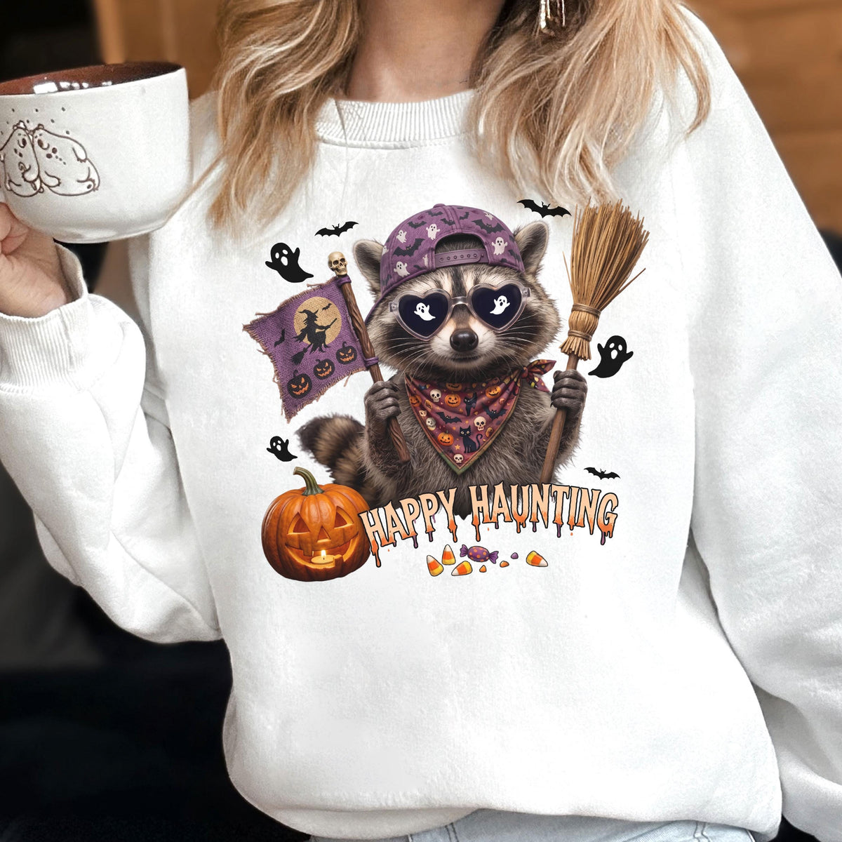 May include: A white crewneck sweatshirt featuring a graphic of a raccoon wearing a purple baseball cap, heart-shaped sunglasses with ghost reflections, and a patterned bandana. The raccoon holds a broom and a flag with a witch silhouette.