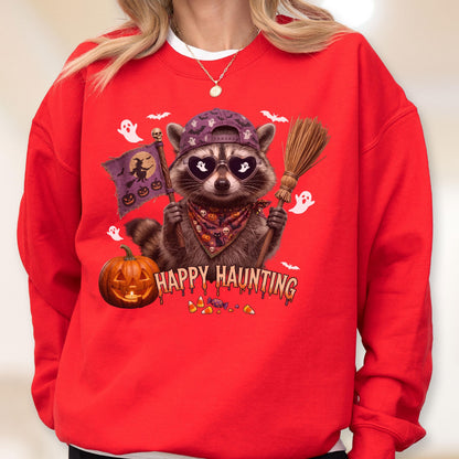 May include: A bright red crewneck sweatshirt featuring a graphic of a raccoon wearing a purple baseball cap, heart-shaped sunglasses, and a patterned bandana. The raccoon holds a broom and a flag with a witch, while the text reads Happy Haunting.