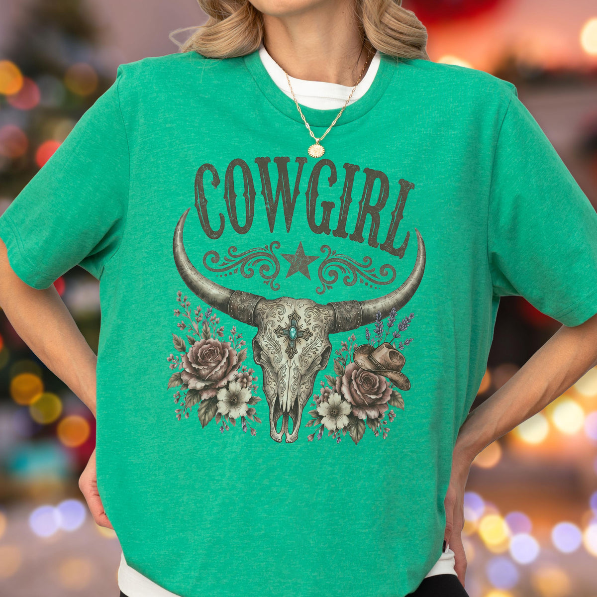 May include: A bright green short-sleeve t-shirt featuring the text COWGIRL in a dark font above a graphic of a longhorn skull, a star, roses, and a cowboy hat. The skull design includes intricate patterns and a small blue center accent.