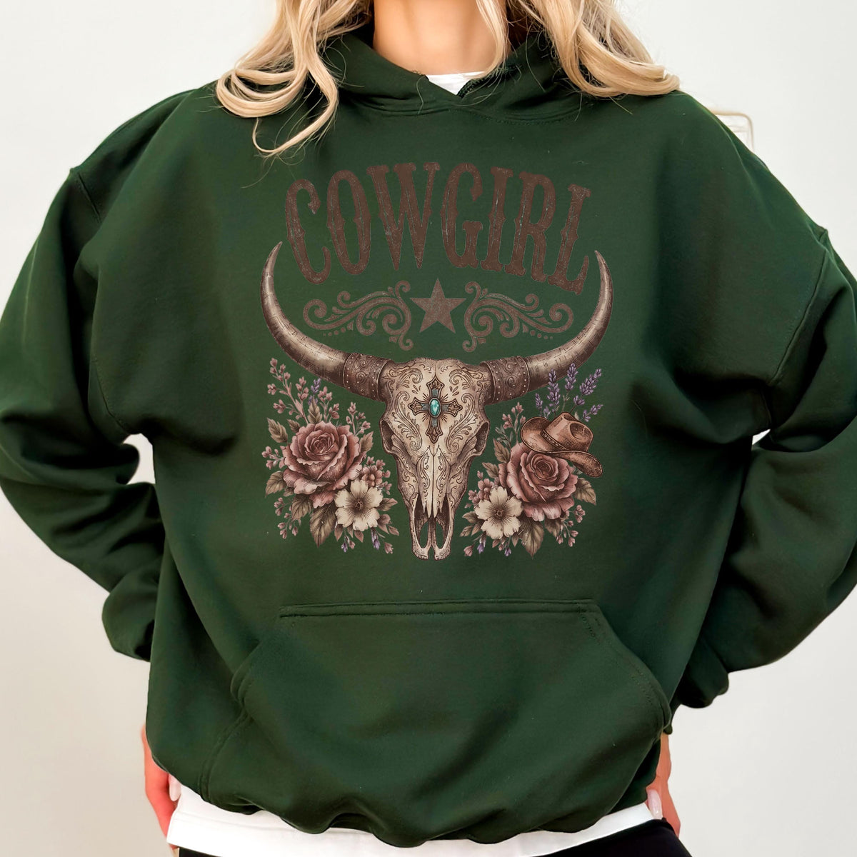 May include: A dark forest green hooded sweatshirt featuring a graphic print of a longhorn steer skull centered on the chest. The skull is surrounded by roses and a cowboy hat, with the word COWGIRL printed in a distressed brown font above.