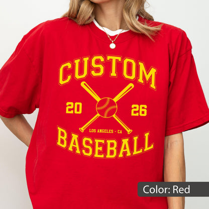 May include: A red short-sleeved t-shirt featuring a yellow graphic with the text CUSTOM BASEBALL, the numbers 20 and 26, and an illustration of two crossed baseball bats with a baseball in the center, plus the text LOS ANGELES - CA.