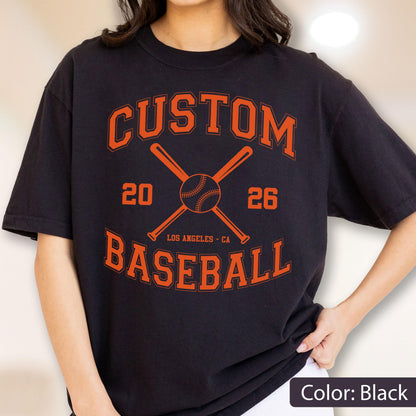 May include: A black t-shirt featuring an orange graphic with the text CUSTOM BASEBALL, the numbers 20 and 26, the words LOS ANGELES - CA, and an illustration of two crossed baseball bats behind a baseball centered on the chest.