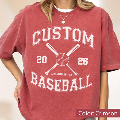 May include: A crimson short-sleeve t-shirt featuring a white graphic print with the text CUSTOM BASEBALL, the numbers 20 and 26, and an illustration of two crossed baseball bats with a baseball in the center, including the text LOS ANGELES - CA.