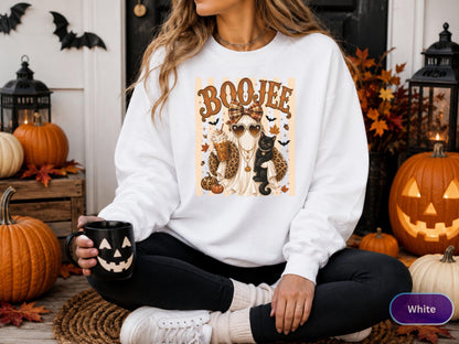 May include: A white long-sleeve sweatshirt featuring a graphic print of a ghost wearing a plaid bow, heart-shaped sunglasses, and a leopard print shawl, holding a coffee cup and a black cat, with the text BOOJEE printed above the ghost.