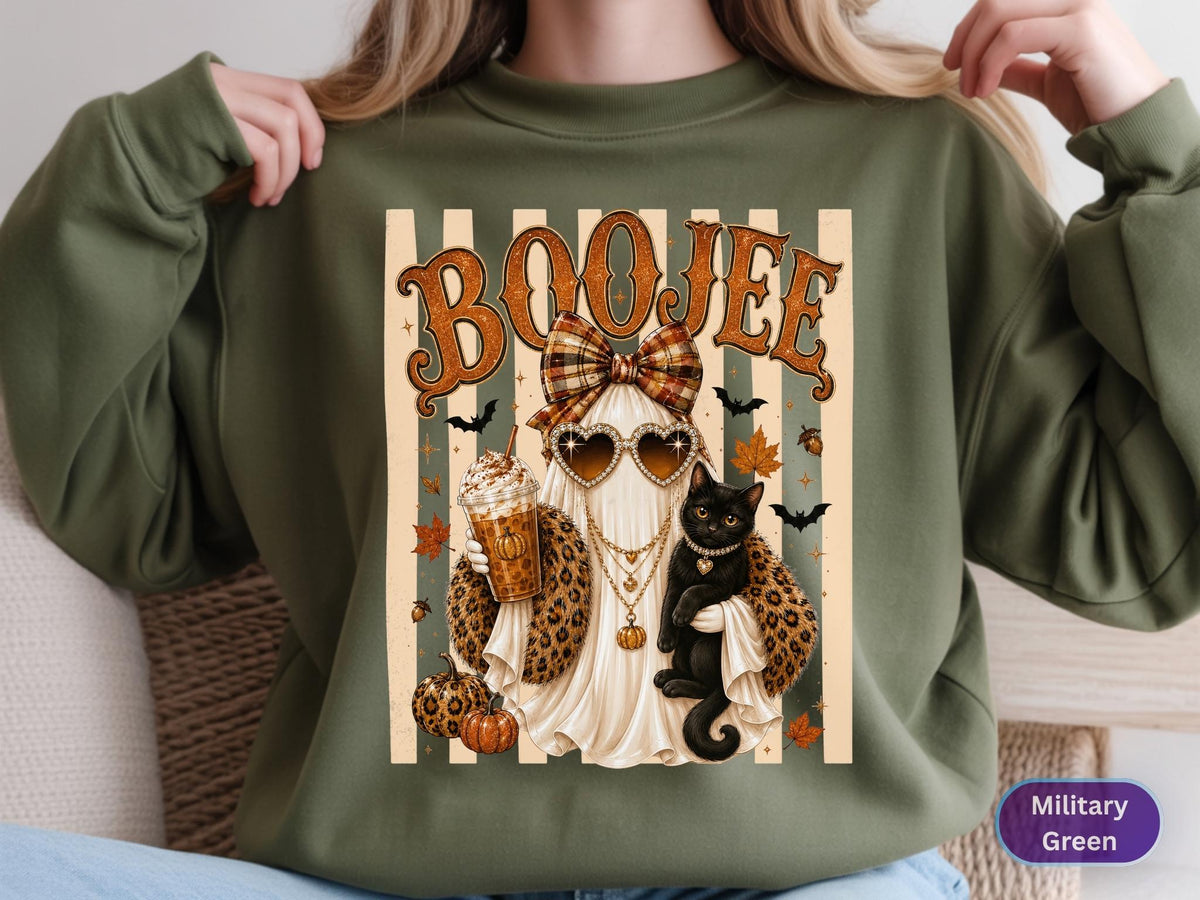 May include: A military green sweatshirt featuring a graphic of a ghost wearing heart-shaped sunglasses, a plaid bow, and a leopard print scarf. The ghost holds an iced coffee and a black cat. The text BOOJEE is printed above, with pumpkins, bats, and leaves.