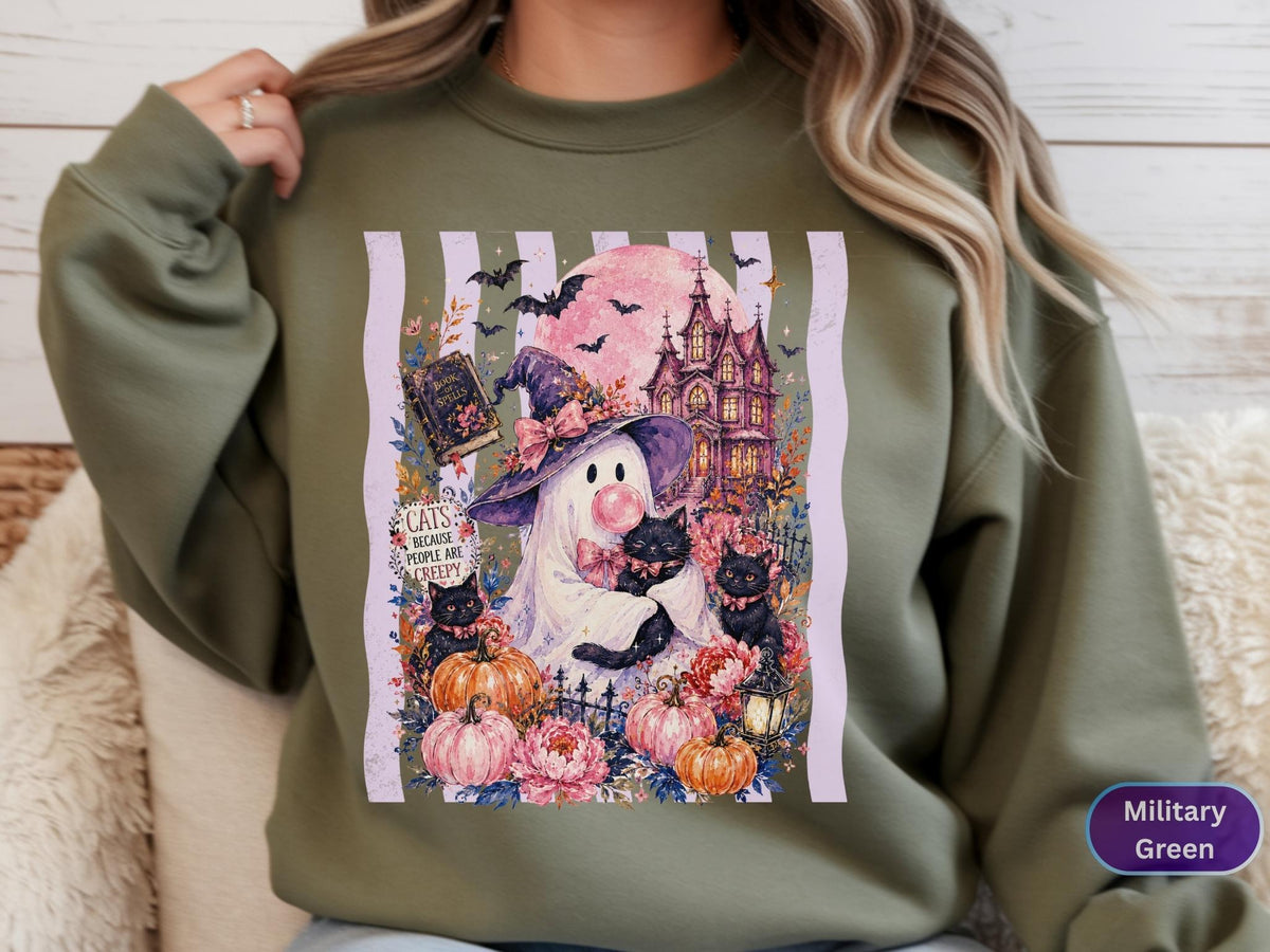May include: A military green sweatshirt featuring a graphic print of a ghost wearing a purple witch hat and blowing a pink bubble. The design includes black cats, pumpkins, a haunted house, a full moon, and text that reads Cats Because People Are Creepy.