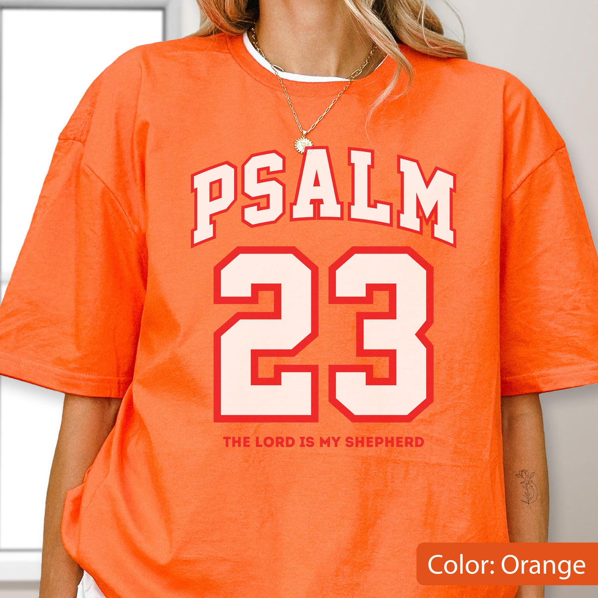 May include: An orange short-sleeve t-shirt featuring the white text PSALM 23 in a collegiate font, with the number 23 in large white block lettering below it, and the text THE LORD IS MY SHEPHERD printed in smaller orange letters underneath.