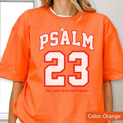 May include: An orange short-sleeve t-shirt featuring the white text PSALM 23 in a collegiate font, with the number 23 in large white block lettering below it, and the text THE LORD IS MY SHEPHERD printed in smaller orange letters underneath.