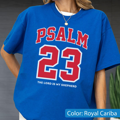 May include: A royal blue short-sleeve t-shirt featuring the red text PSALM 23 in a collegiate font, with the number 23 in large red digits below it, and the white text THE LORD IS MY SHEPHERD printed in a smaller font at the bottom center.