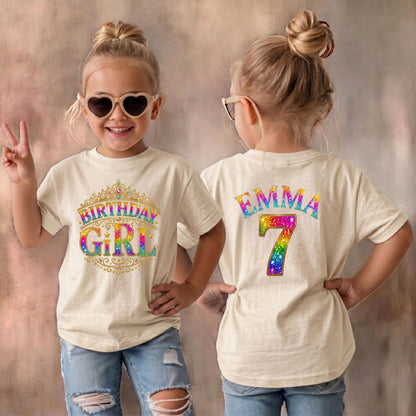 May include: A cream-colored t-shirt featuring a front graphic of a gold crown with the text "BIRTHDAY GIRL" in rainbow colors. The back of the shirt displays the name "EMMA" in rainbow letters above a large rainbow-colored number "7" with sparkles.
