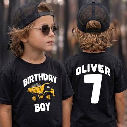 May include: A black t-shirt featuring a yellow dump truck graphic with the text "BIRTHDAY BOY" on the front and the name "OLIVER" above the number "7" on the back. The shirt is paired with a black mesh trucker hat and round sunglasses.