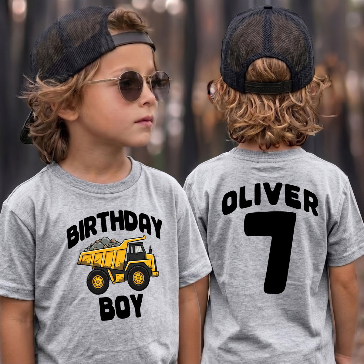 May include: A heather gray t-shirt featuring a yellow dump truck graphic with the text "BIRTHDAY BOY" on the front and the name "OLIVER" above the number "7" on the back, paired with a black mesh trucker hat and round sunglasses.