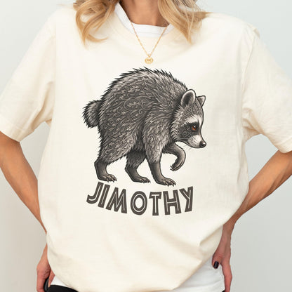 May include: A cream-colored short-sleeve t-shirt featuring a detailed illustration of a raccoon with intricate leaf-like patterns on its fur. Below the raccoon, the text JIMOTHY is printed in a bold, dark, sans-serif font on the front center.