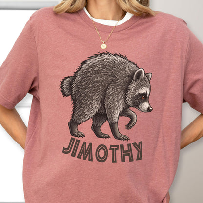 May include: A dusty rose t-shirt featuring a graphic illustration of a raccoon with intricate leaf-like patterns in its fur. Below the raccoon, the name JIMOTHY is printed in bold, dark brown capital letters. The shirt has a crew neckline.