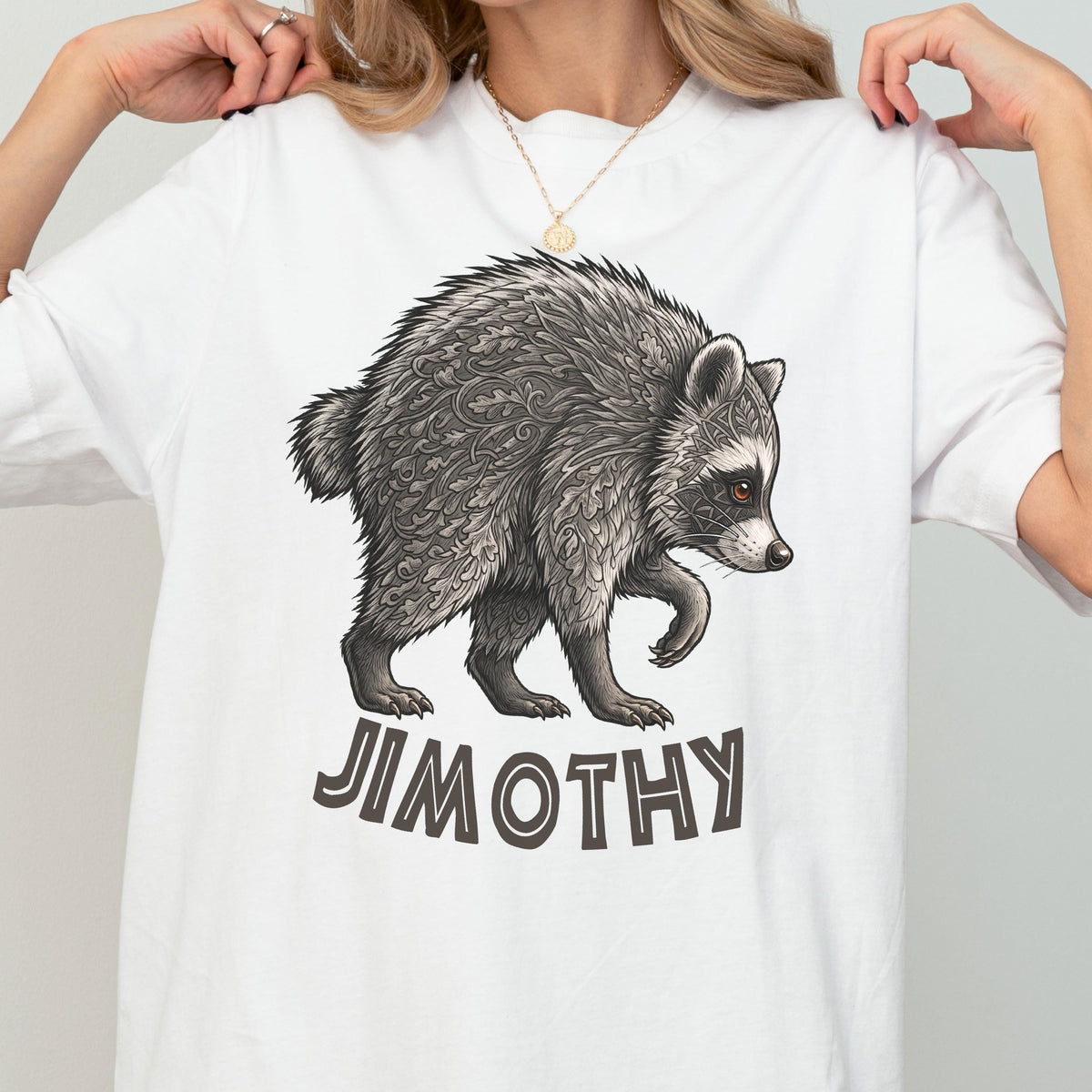 May include: A white short-sleeved t-shirt featuring a graphic illustration of a raccoon with intricate leaf-like patterns in its fur. Below the raccoon, the name JIMOTHY is printed in bold, dark gray capital letters. The design is centered on the chest.