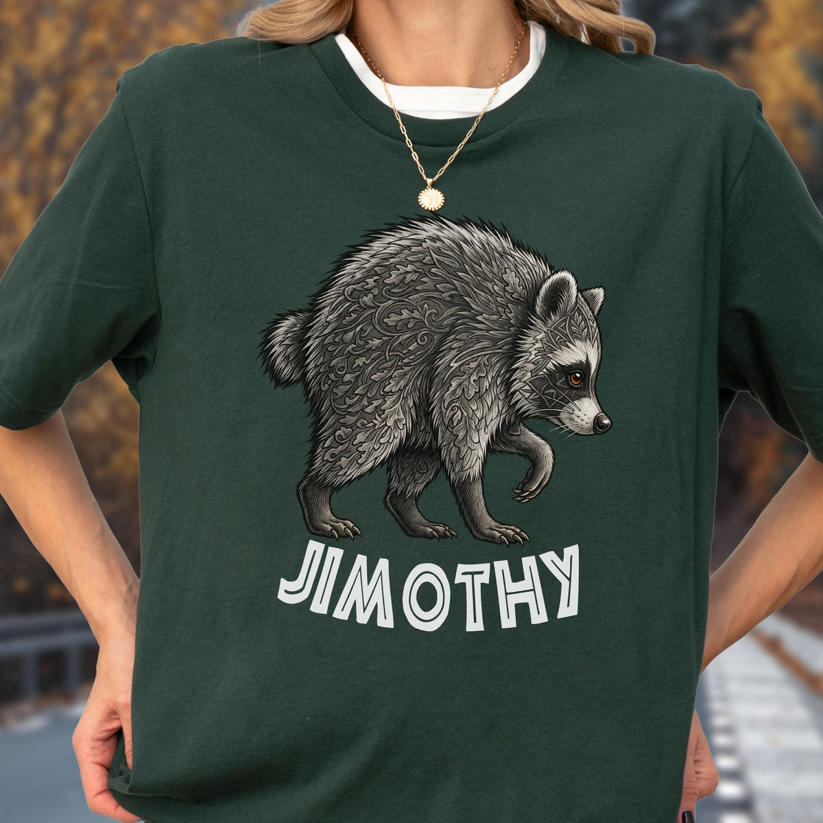 May include: A dark green short-sleeved t-shirt featuring a detailed graphic of a raccoon with intricate leaf-like patterns in its fur. Below the raccoon, the name JIMOTHY is printed in bold, white, sans-serif capital letters on the chest.