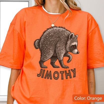 May include: A bright orange short-sleeve t-shirt featuring a graphic of a raccoon with intricate leaf-like patterns in its fur. Below the raccoon, the text JIMOTHY is printed in a dark brown, bold, sans-serif font. The shirt has a crew neckline.