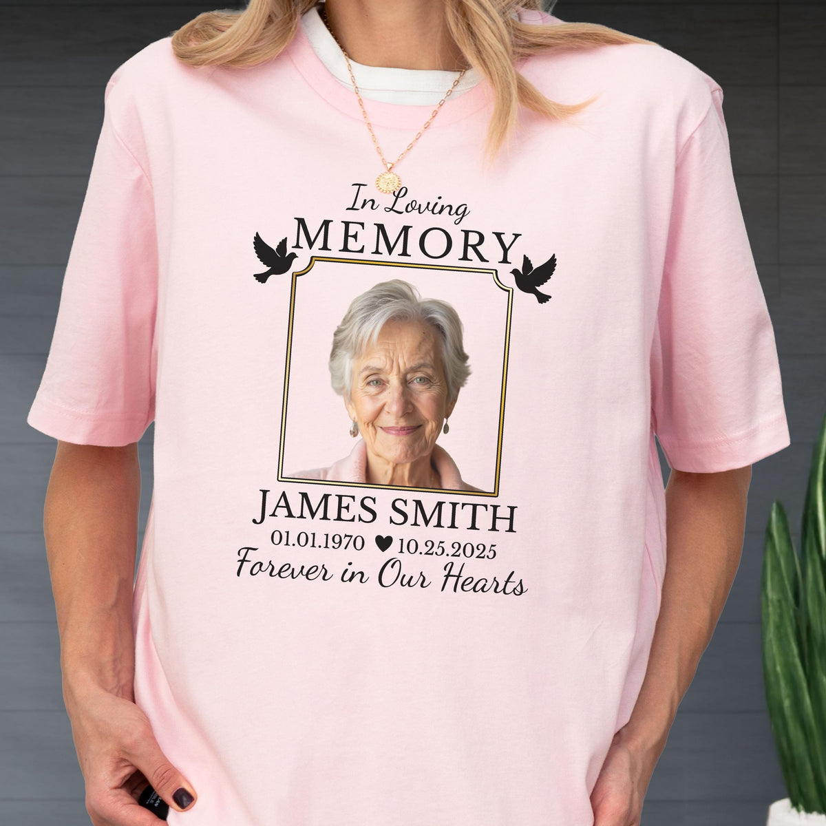 May include: A light pink short-sleeve t-shirt featuring a memorial graphic with a portrait of an older person inside a gold frame. The text reads In Loving Memory, JAMES SMITH, 01.01.1970, 10.25.2025, and Forever in Our Hearts with two black doves.