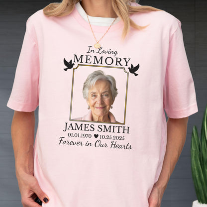 May include: A light pink short-sleeve t-shirt featuring a memorial graphic with a portrait of an older person inside a gold frame. The text reads In Loving Memory, JAMES SMITH, 01.01.1970, 10.25.2025, and Forever in Our Hearts with two black doves.