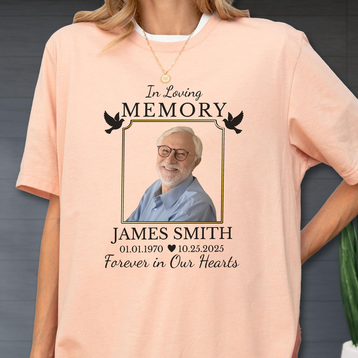 May include: A peach-colored t-shirt featuring a memorial graphic with the text In Loving Memory, a photograph of a man wearing glasses, the name JAMES SMITH, the dates 01.01.1970 and 10.25.2025 with a heart symbol, and the text Forever in Our Hearts.