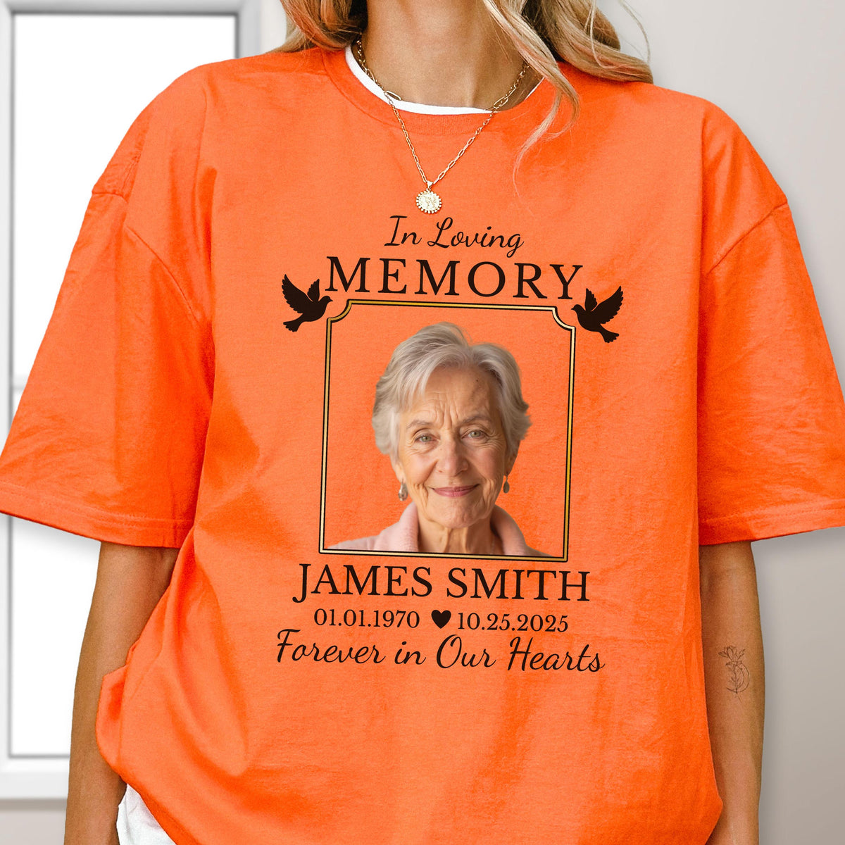 May include: A bright orange t-shirt featuring a memorial graphic with the text In Loving Memory, a photograph of an older person, the name James Smith, the dates 01.01.1970 and 10.25.2025 separated by a heart, and the phrase Forever in Our Hearts.