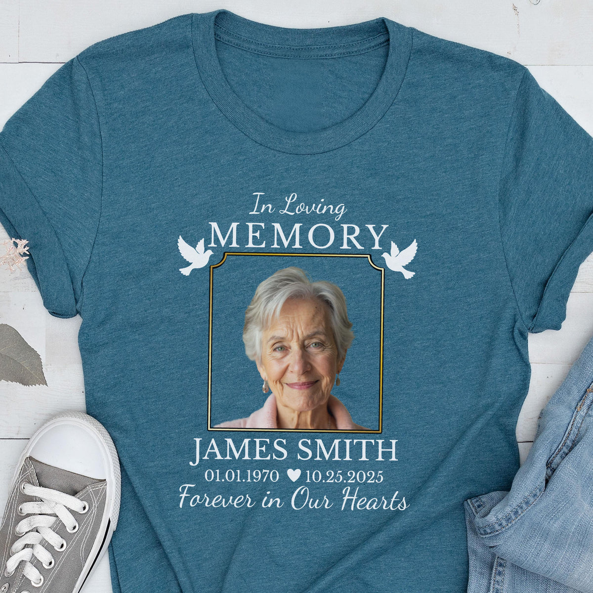 May include: A teal blue crew neck t-shirt featuring a memorial graphic with the text In Loving Memory, the name James Smith, dates 01.01.1970 and 10.25.2025, and the phrase Forever in Our Hearts, surrounding a portrait of an older person with white hair.