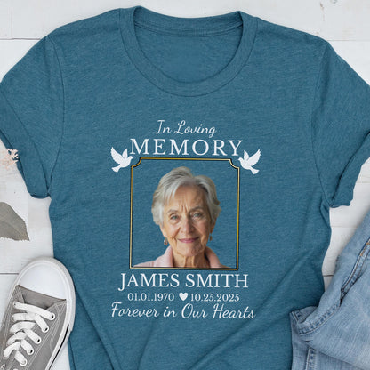 May include: A teal blue crew neck t-shirt featuring a memorial graphic with the text In Loving Memory, the name James Smith, dates 01.01.1970 and 10.25.2025, and the phrase Forever in Our Hearts, surrounding a portrait of an older person with white hair.