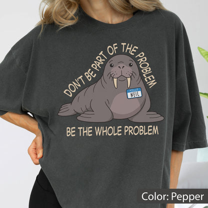 May include: A pepper-colored t-shirt featuring a graphic of a walrus wearing a name tag that reads "HELLO NEIL". The text above the walrus says "DON'T BE PART OF THE PROBLEM" and the text below the walrus says "BE THE WHOLE PROBLEM" in light tan.