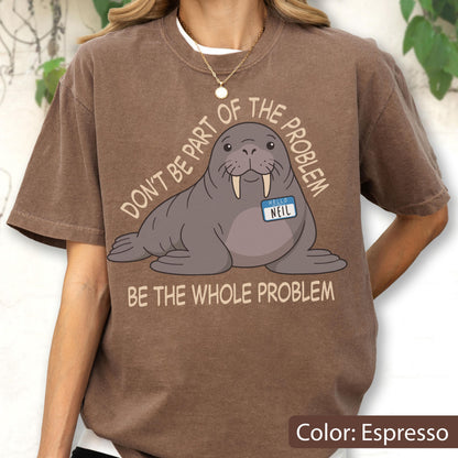 May include: An espresso-colored t-shirt featuring a cartoon walrus with a name tag that reads "HELLO NEIL". The text above the walrus says "DON'T BE PART OF THE PROBLEM" and the text below the walrus says "BE THE WHOLE PROBLEM" in light tan.