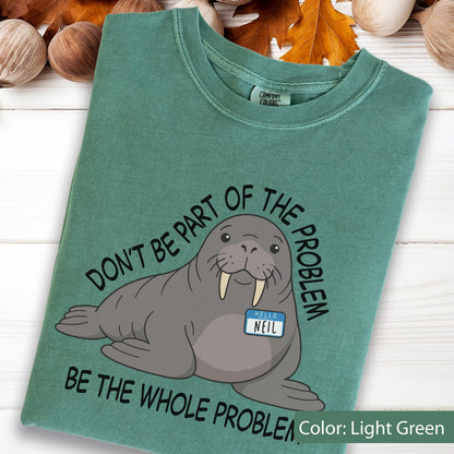 May include: A light green t-shirt featuring a graphic of a gray walrus wearing a blue name tag that reads "HELLO NEIL". The text "DON'T BE PART OF THE PROBLEM" is arched above the walrus, and "BE THE WHOLE PROBLEM" is printed below it in black.