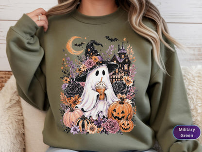 May include: A military green crewneck sweatshirt featuring a graphic print of a white ghost wearing a witch hat, holding a coffee cup, surrounded by pumpkins, flowers, bats, a crescent moon, and a dark house silhouette in a fall theme.
