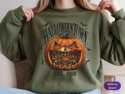 May include: A military green crewneck sweatshirt featuring a large orange jack-o'-lantern graphic. Inside the pumpkin is a detailed scene of a town with a clock tower and a full moon. The text reads HALLOWEENTOWN and EST. 1998 in black lettering.