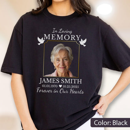 May include: A black t-shirt featuring a memorial design with a photograph of an older person. The text reads In Loving MEMORY, JAMES SMITH, 01.01.1970, 10.25.2025, and Forever in Our Hearts, accompanied by two white dove illustrations.