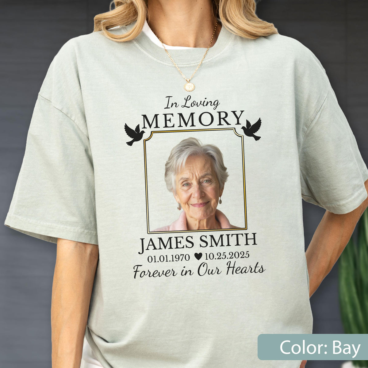 May include: A bay-colored t-shirt featuring a memorial graphic with the text In Loving MEMORY, JAMES SMITH, 01.01.1970, 10.25.2025, and Forever in Our Hearts. The design includes a framed photograph of an older person and two black bird silhouettes.