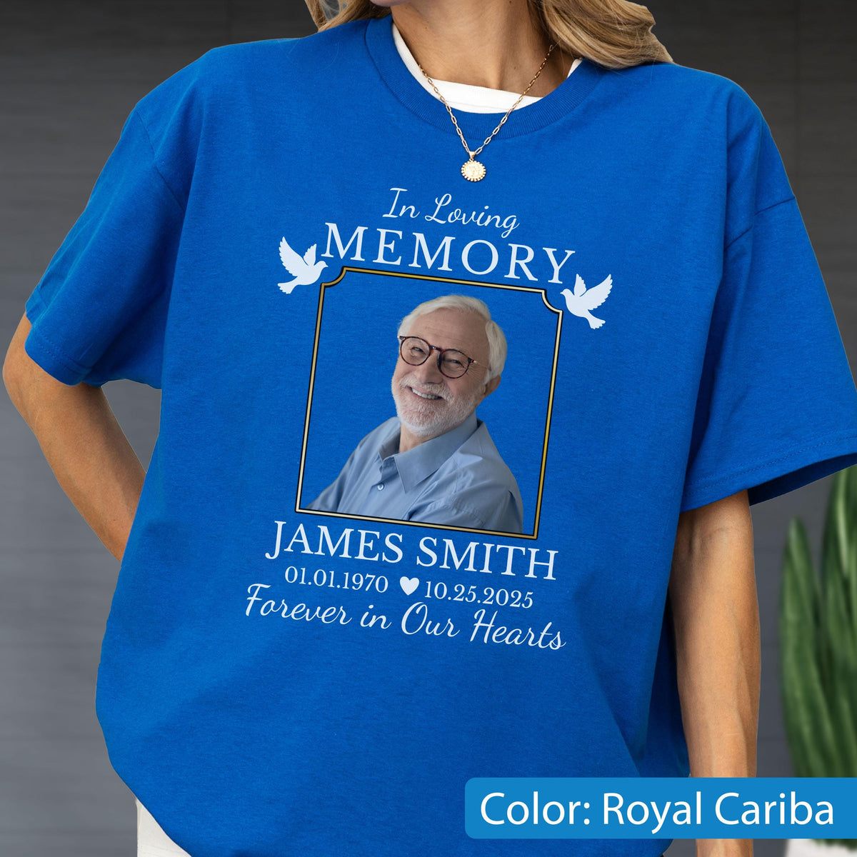 May include: A royal blue t-shirt featuring a memorial graphic with the text In Loving Memory, James Smith, 01.01.1970, 10.25.2025, and Forever in Our Hearts. The design includes a framed photograph of an older person with glasses and white doves.