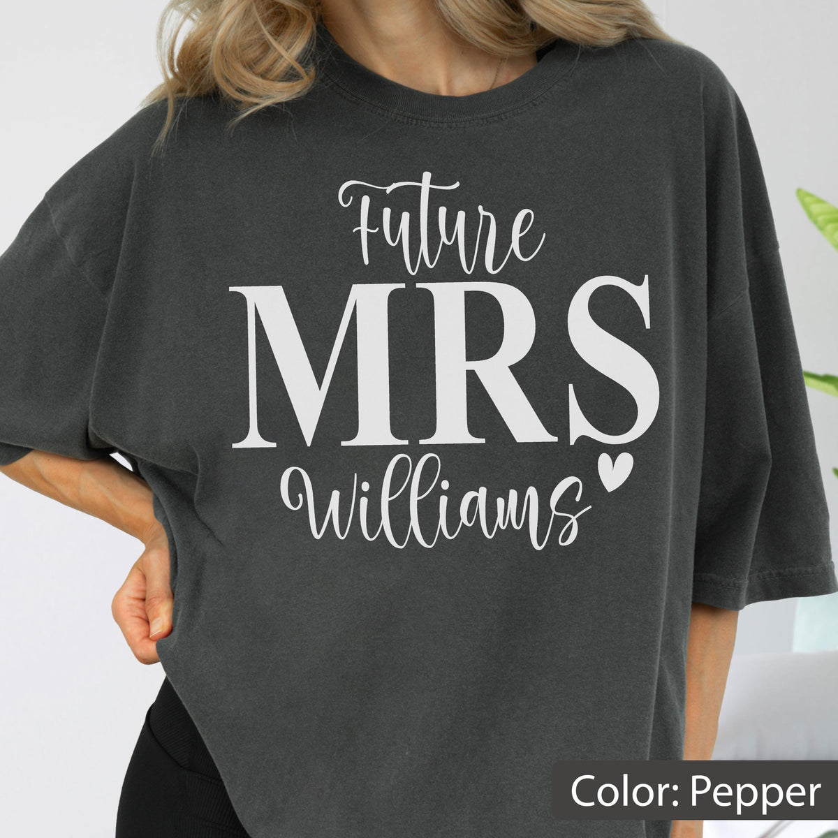 May include: A charcoal gray short-sleeved t-shirt featuring white screen-printed text that reads Future MRS Williams with a small heart icon. The shirt has a relaxed fit and a crew neckline, showcasing a solid dark pepper-colored fabric.