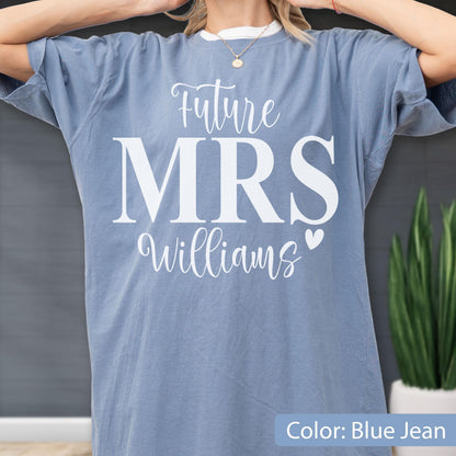 May include: A blue jean colored t-shirt featuring white screen-printed text that reads Future MRS Williams with a small heart icon. The shirt has a crew neckline and short sleeves, displaying a casual fit with a solid, muted blue fabric finish.