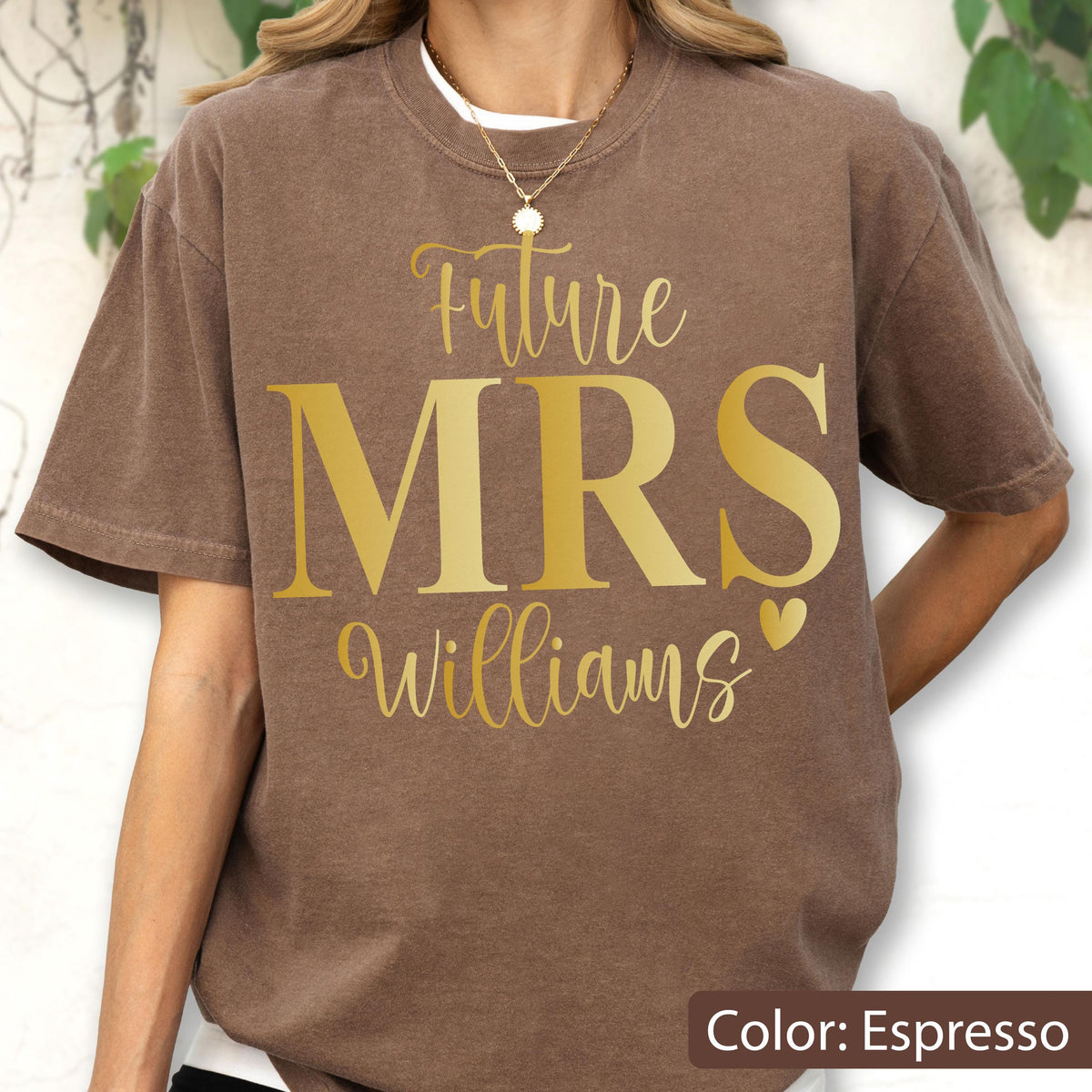 May include: An espresso brown short-sleeve t-shirt featuring gold text that reads Future MRS Williams with a small heart icon. The shirt has a crew neckline and a relaxed fit, showcasing a screen-printed design centered on the chest area.