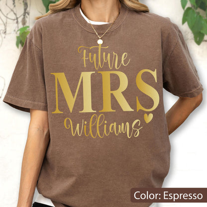 May include: An espresso brown short-sleeve t-shirt featuring gold text that reads Future MRS Williams with a small heart icon. The shirt has a crew neckline and a relaxed fit, showcasing a screen-printed design centered on the chest area.