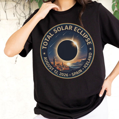 May include: A black t-shirt featuring a circular graphic of a total solar eclipse over a coastal town. The text reads TOTAL SOLAR ECLIPSE, AUGUST 12, 2026, SPAIN, ICELAND. The design includes a dark sun, a bright corona, and falling stars.
