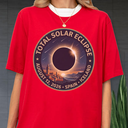May include: A bright red t-shirt featuring a circular graphic of a total solar eclipse over a coastal town. The text reads Total Solar Eclipse, August 12, 2026, Spain, Iceland. The design includes a dark sun, a bright corona, and stars.